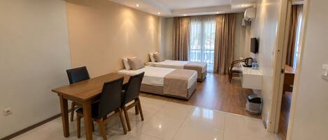 A hotel room with a dining table, two beds, a small kitchenette, and a bathroom.