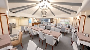 A hotel dining area with multiple tables and chairs, a chandelier, and a kitchen in the background. - VILLA LYCUS TERMAL OTEL (Denizli)