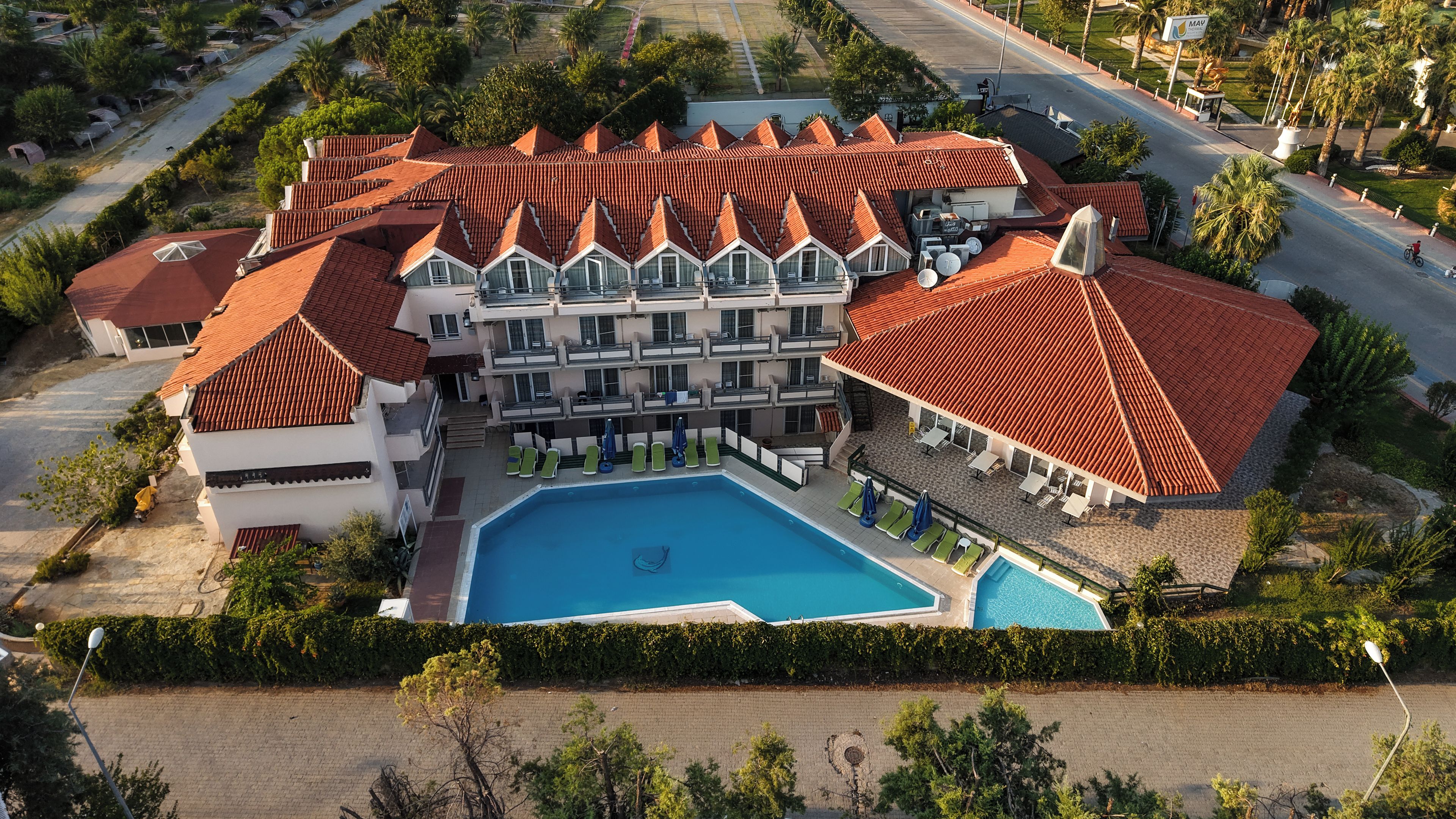 A hotel with a swimming pool, multiple balconies, and a red-tiled roof.