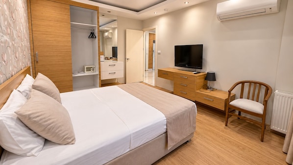 Quarto de hotel com cama, cómoda de madeira, televisão, cadeira e radiador.