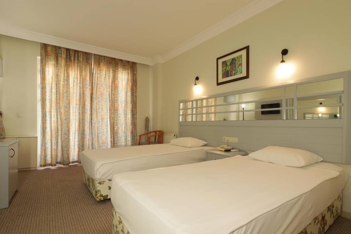 A hotel room with two beds, a desk, a chair, a mirror, and a window with curtains.