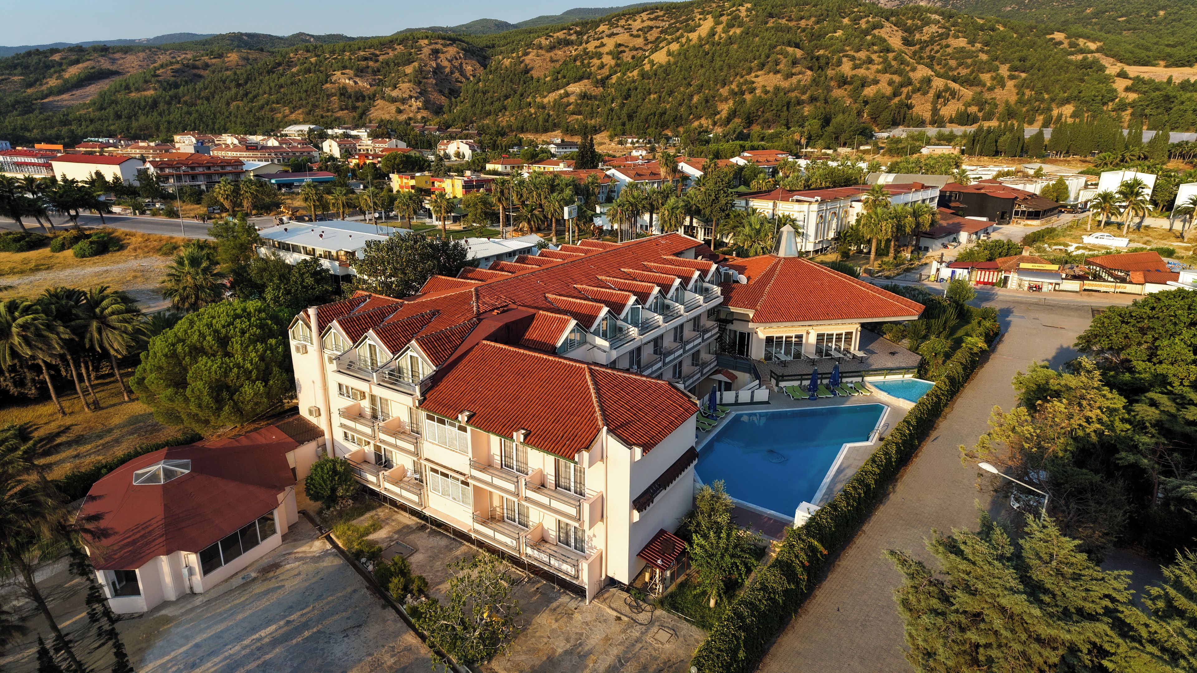 A large hotel with multiple floors, a swimming pool, and a view of the surrounding hills.