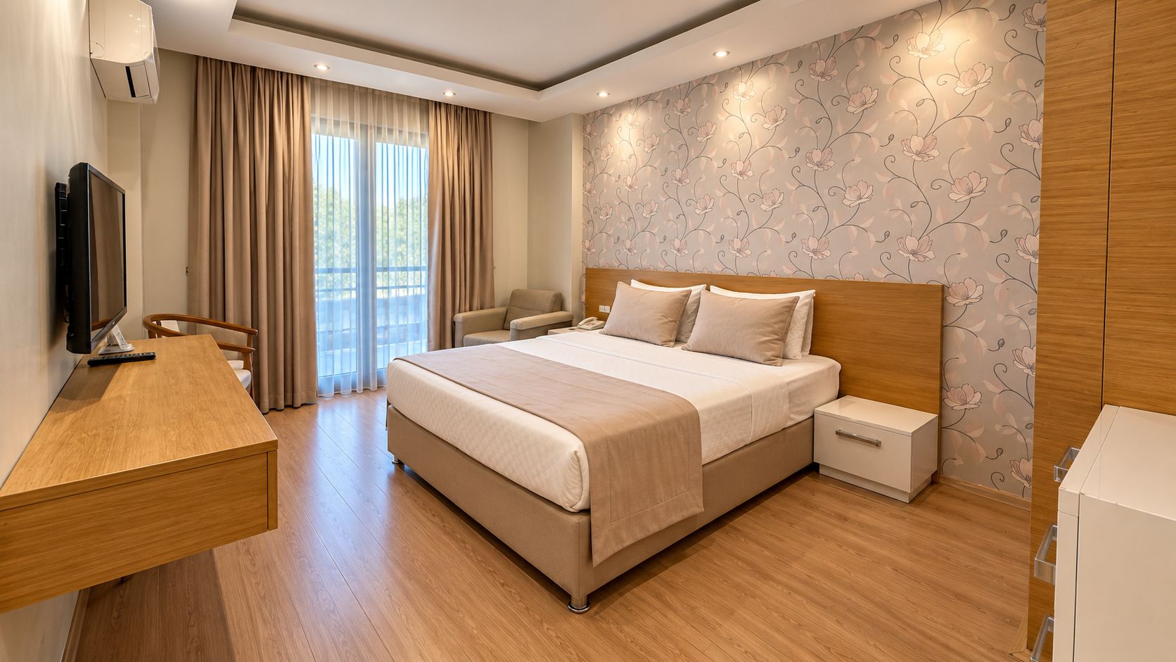Quarto de hotel com cama, mesas de cabeceira, escrivaninha, cadeira e televisão.
