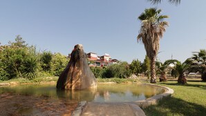 A water feature with a stone structure, surrounded by greenery and a building in the background. - VILLA LYCUS TERMAL OTEL (Denizli)