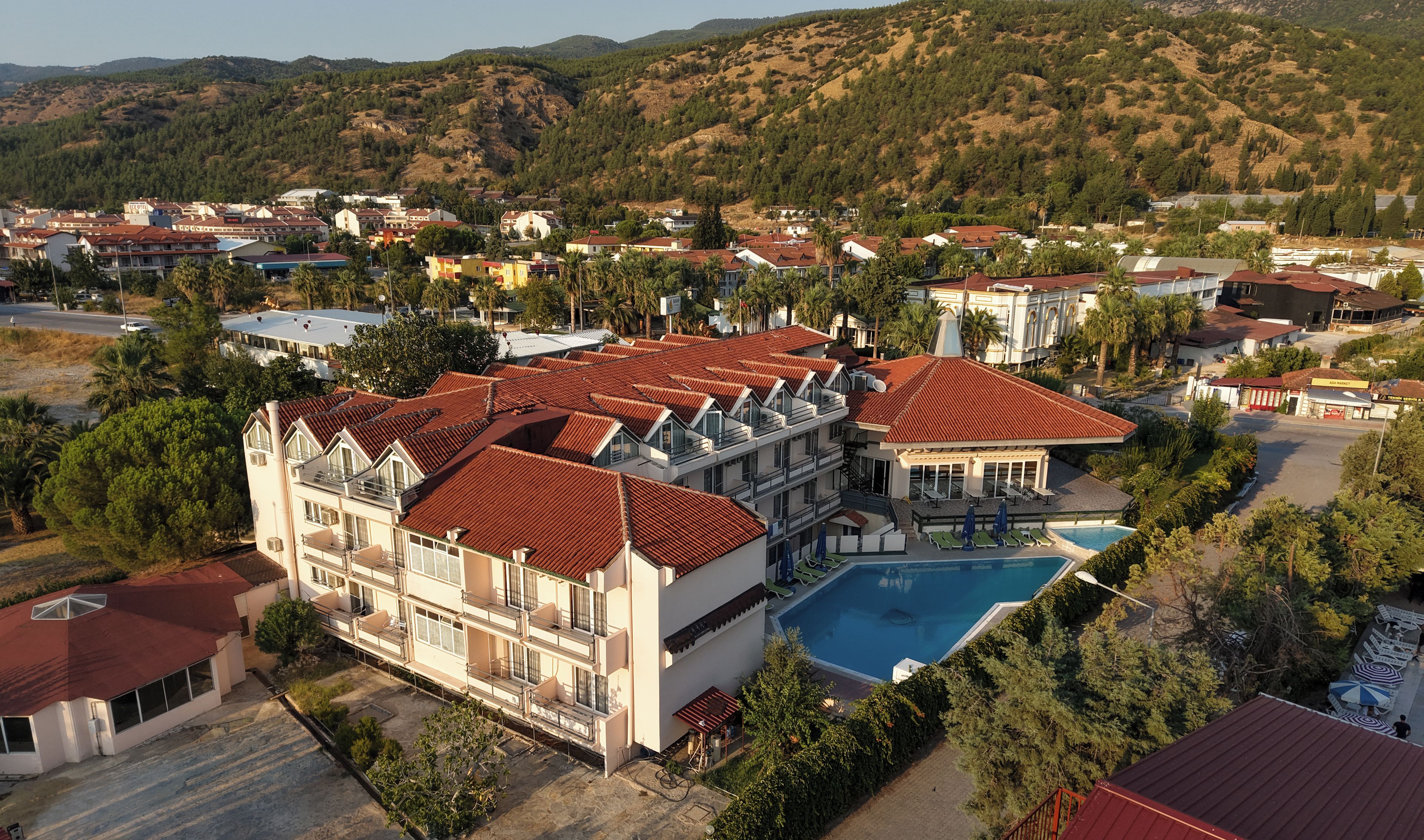A hotel with multiple balconies, a swimming pool, and a view of the surrounding hills.