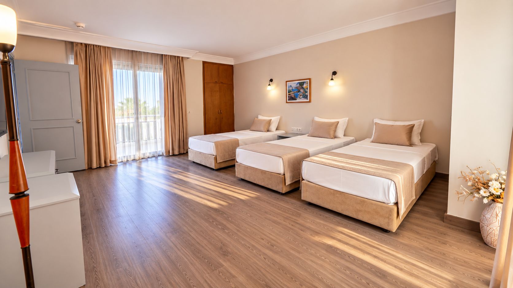 A hotel room with a wooden floor, two beds, a wardrobe, a desk, and a lamp.