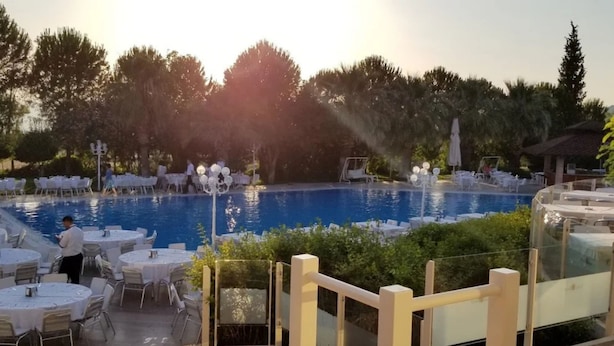 A poolside area with tables and chairs, a pool, and surrounding greenery. - VILLA LYCUS TERMAL OTEL (Denizli)