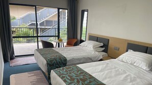 Ein Hotelzimmer mit zwei Betten, einem kleinen Tisch und einem Stuhl. Blick auf einen Balkon und ein Gebäude.