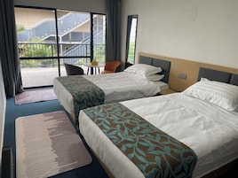 Habitación de hotel con dos camas, una mesita y una silla. Se ve un balcón y un edificio desde el exterior.