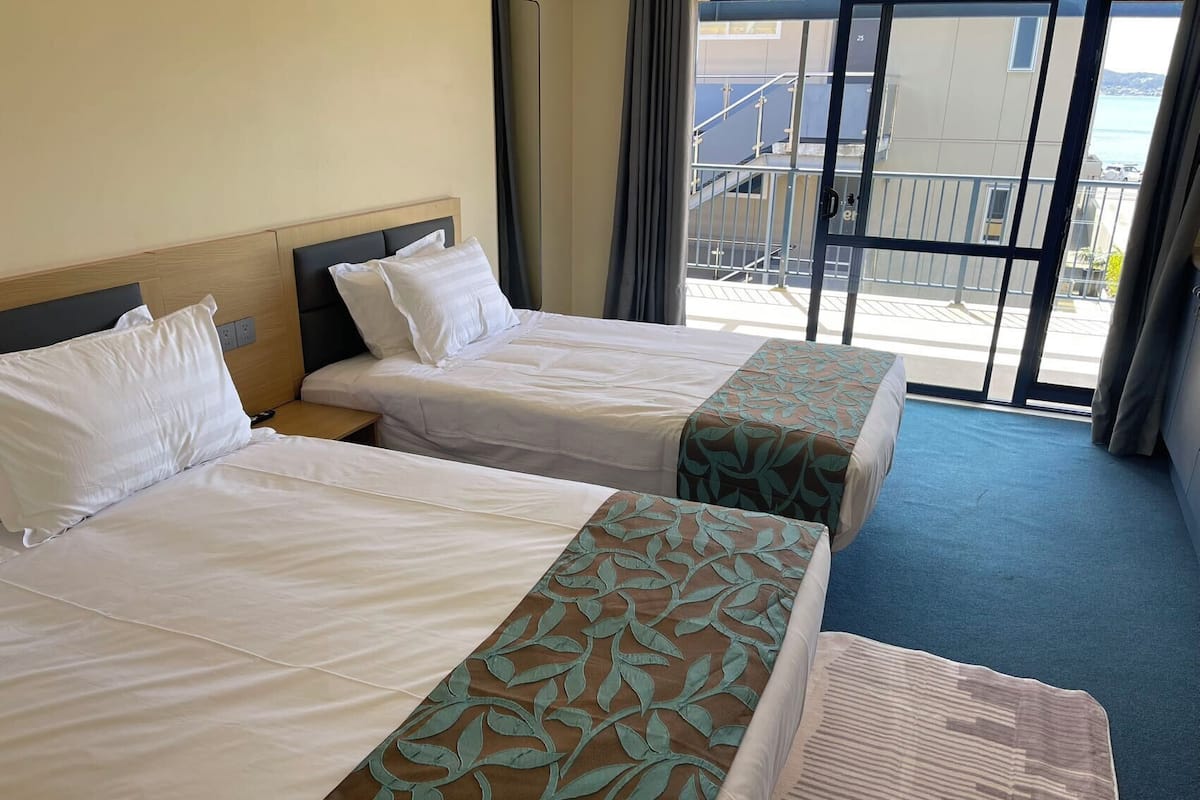 A hotel room with two beds, a window with a view of a balcony and buildings, and a blue carpet.