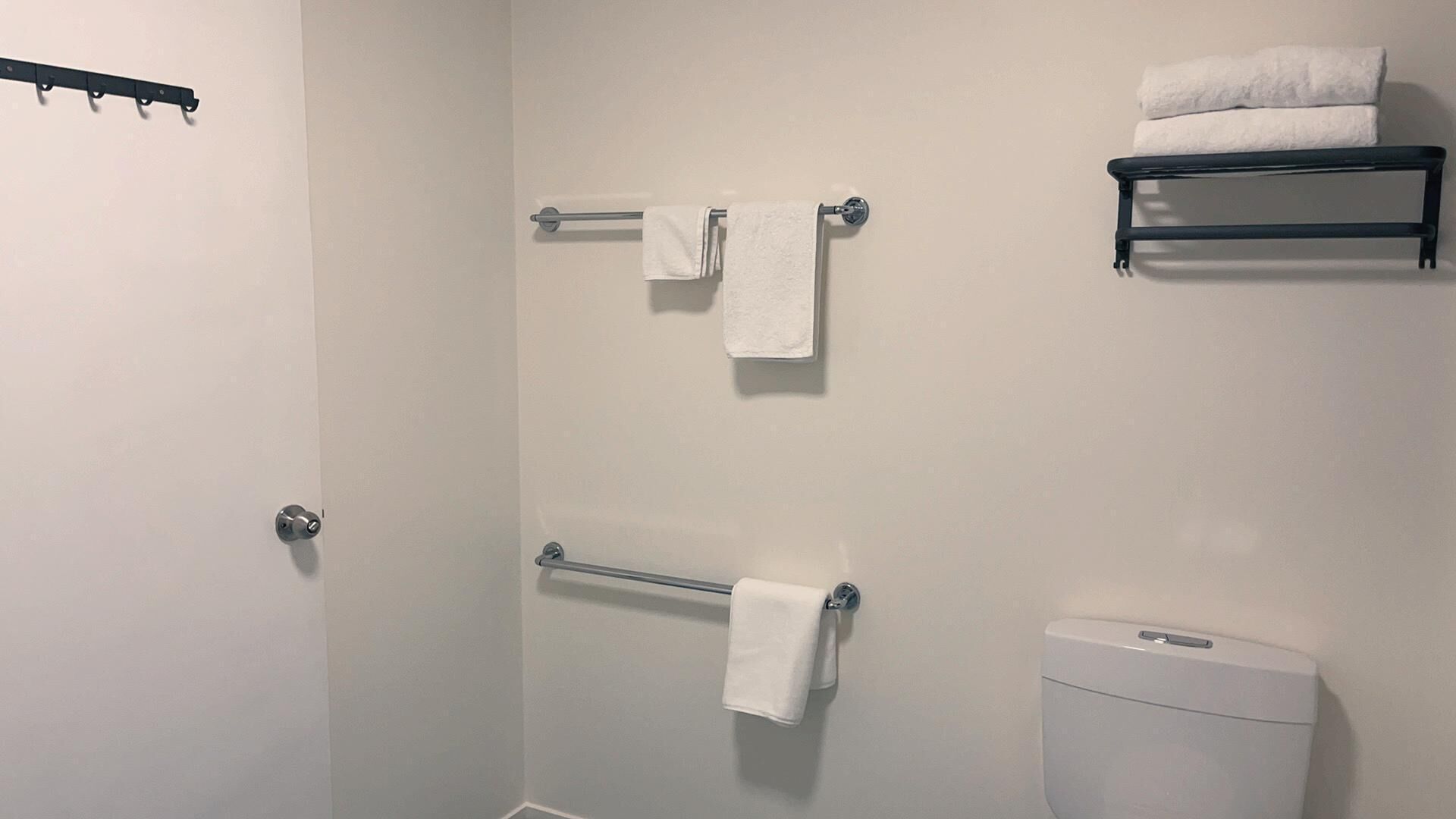 A bathroom with a toilet, two towel bars with towels, and a towel rack.