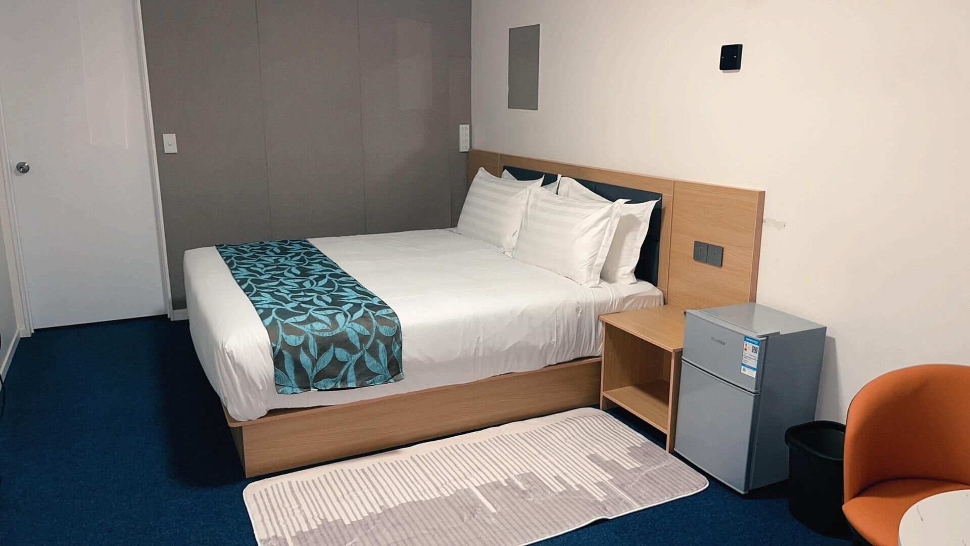 A hotel room with a bed, a desk, a chair, a small cabinet, and a rug.