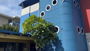 Ein modernes Gebäude mit blauer Fassade, zahlreichen Fenstern und einem Baum davor.