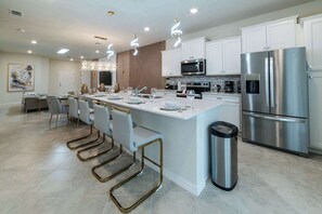 A modern kitchen with white cabinetry, stainless steel appliances, and a central island with bar stools. - FunTastic Themed 5BR Home, Pool & Game Room (Clermont)
