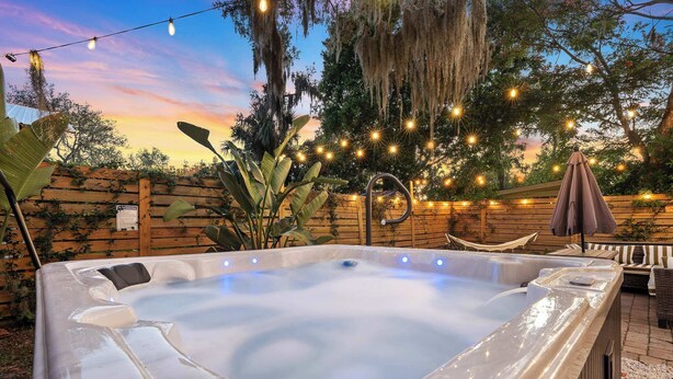 Un bain à remous doté d’une terrasse en bois et illuminé de guirlandes lumineuses, entouré de plantes et d’une clôture en bois.