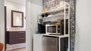 Une cuisine compacte équipée d’un four à micro-ondes, d’un petit réfrigérateur et d’une étagère où sont disposés des objets décoratifs.