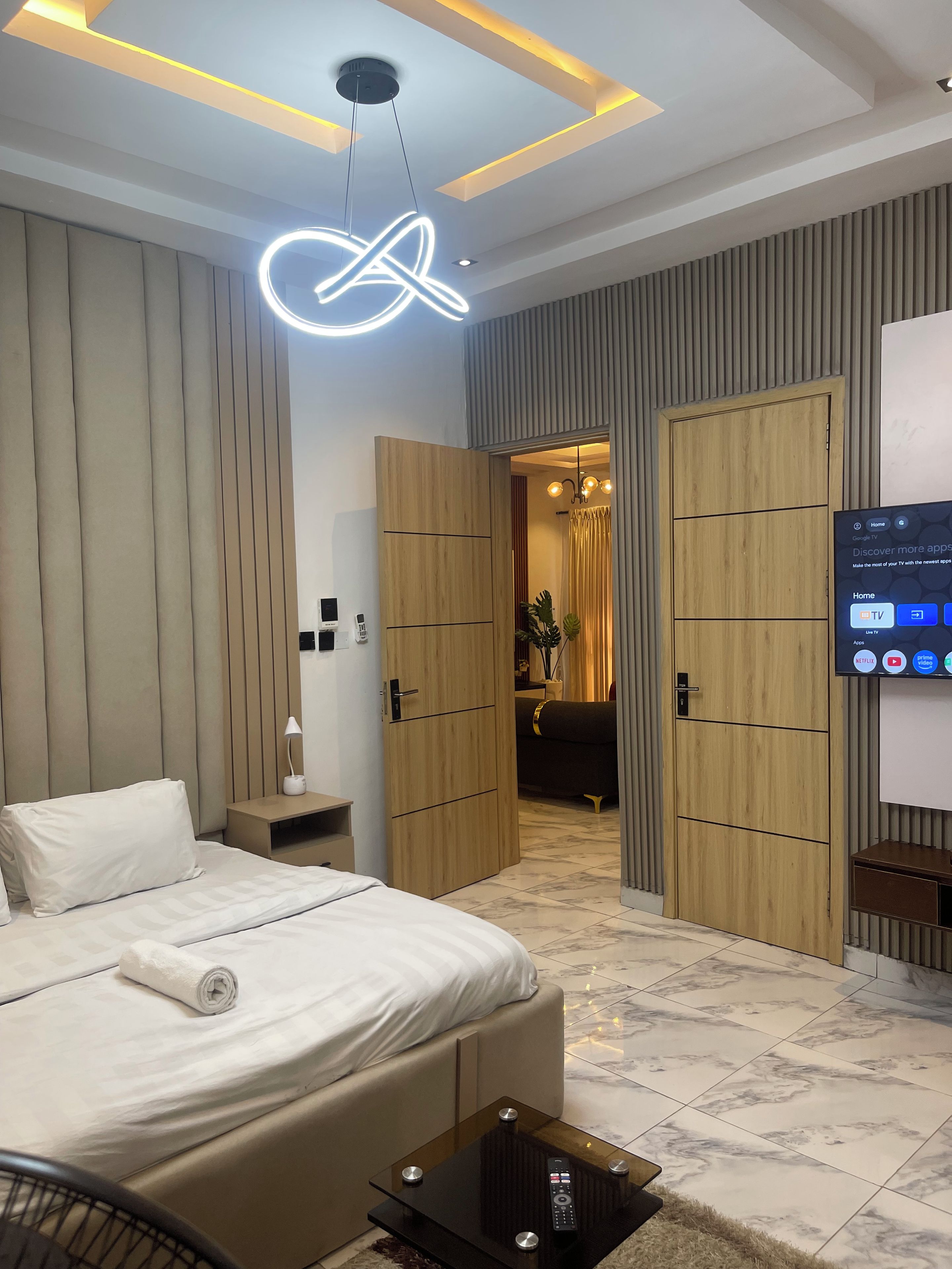 Ein modernes Hotelzimmer mit Bett, Nachttisch und Fernseher, der einen Homescreen anzeigt.