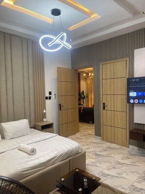 A modern hotel room with a bed, bedside table, and a TV displaying a home screen. - Snowdrop Apartments  (Lekki)