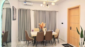 A dining area with a marble floor, a table with chairs, a chandelier, and a wooden door. - Snowdrop Apartments  (Lekki)