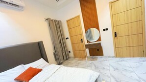 A modern bedroom with a bed, a vanity with a mirror, and two wardrobes. - Snowdrop Apartments  (Lekki)