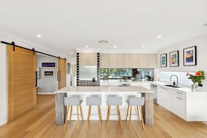 A modern kitchen with a central island, bar stools, and a sliding barn door. - Hibiscus by Coast Hosting (Wamberal)