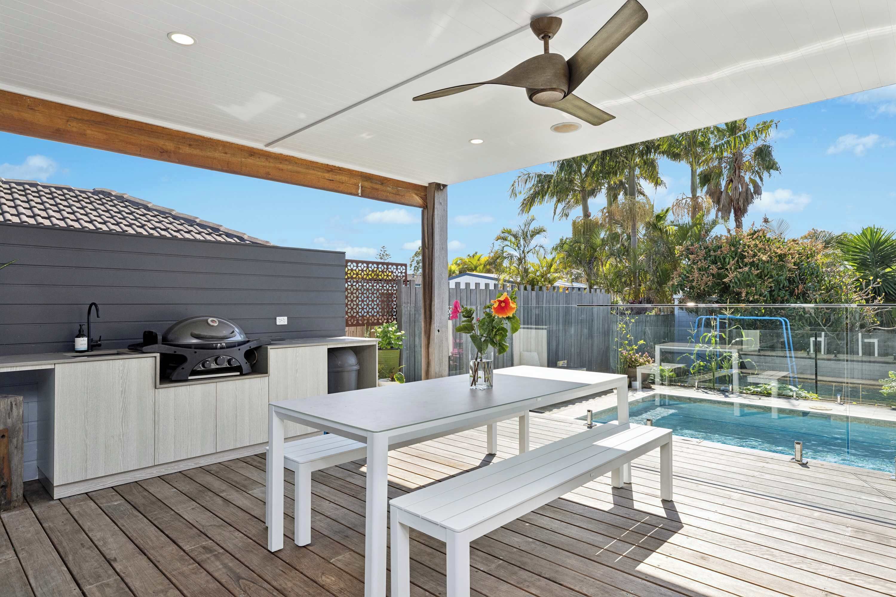 Un patio al aire libre con piscina, una parrilla y una mesa de comedor con bancos.