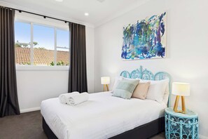 Ein Hotelzimmer mit einem großen Bett, zwei Nachttischlampen, einem fenster mit Vorhängen und einem Wandbild.