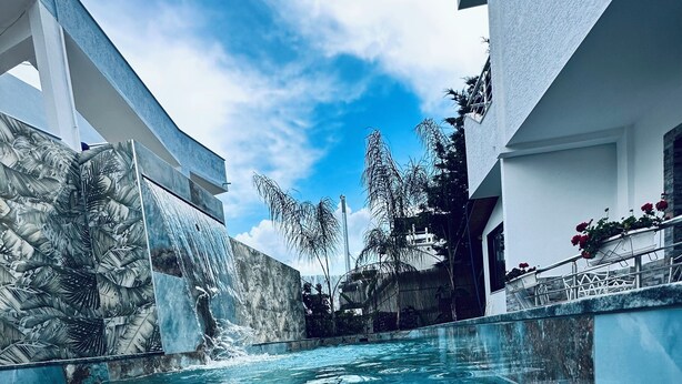 A clear pool with a waterfall feature, surrounded by modern architecture and tropical plants. - Ilio Boutique Swim Up Rooms (Ksamil)