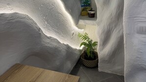 A narrow, white-walled room with a wooden table, a potted plant, and a shelf with two paintings and two small potted plants. - Ilio Boutique Swim Up Rooms (Ksamil)