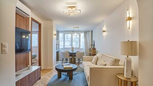 Ett modernt vardagsrum med en soffa, ett soffbord och en lampa. En TV står på ett träskåp, och det finns en matplats med stolar och ett bord.