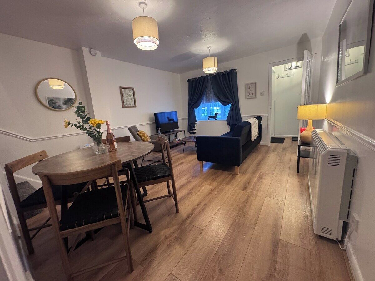 Una sala moderna con comedor, un sofá, un televisor y un ventanal con cortinas.
