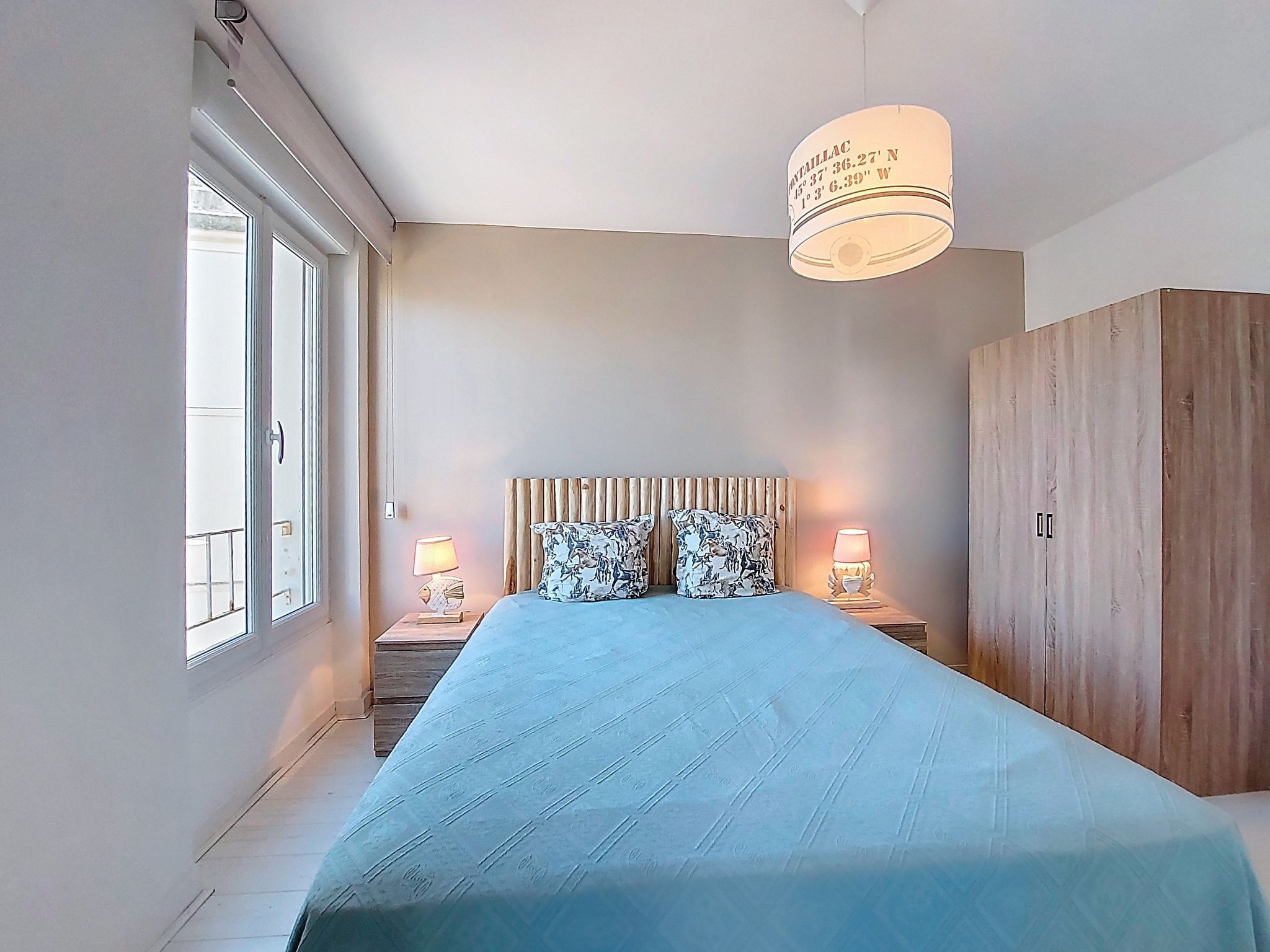 Een slaapkamer met een groot bed, een houten hoofdbord, twee nachtkastjes met lampen en een garderobe.