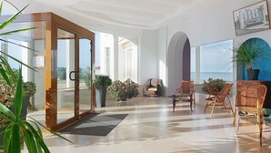 Een ruime woonkamer met een glazen deur, diverse zithoeken en uitzicht op de zee.