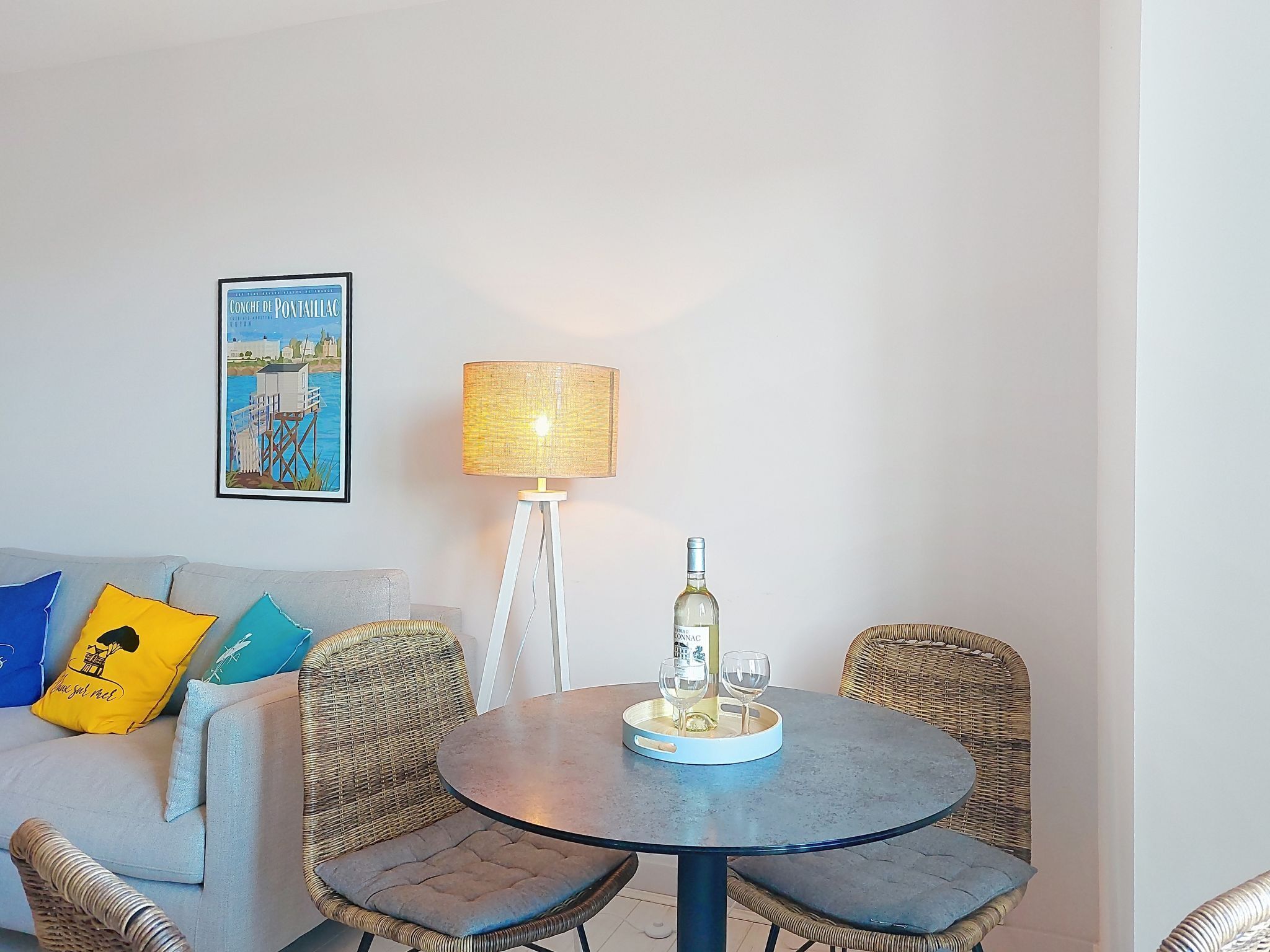 A dining area with wicker chairs, a round table, a bottle of wine, and a lamp.