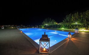 Una piscina nocturna con una escultura de cisne, rodeada de follaje e iluminada por faroles.