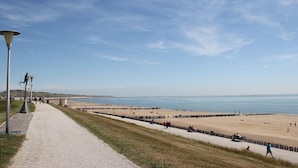 Une promenade en bord de mer qui mène à une plage, avec un ciel dégagé.