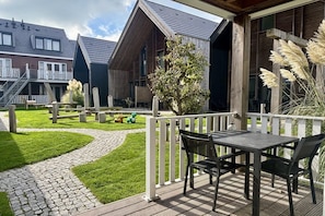 A wooden deck with a table and chairs, a stone pathway, and a fenced garden area with decorative elements. - Beautiful lodge located in center of Zoutelande (Zoutelande)
