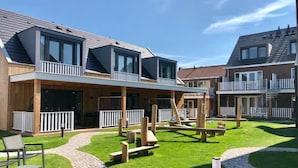 Un bâtiment moderne doté de nombreux balcons, une cour pavée avec des bancs en bois et un ciel dégagé.