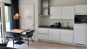 Une cuisine moderne avec des meubles blancs, un four en acier inoxydable et un coin repas comprenant une table en bois et deux chaises.