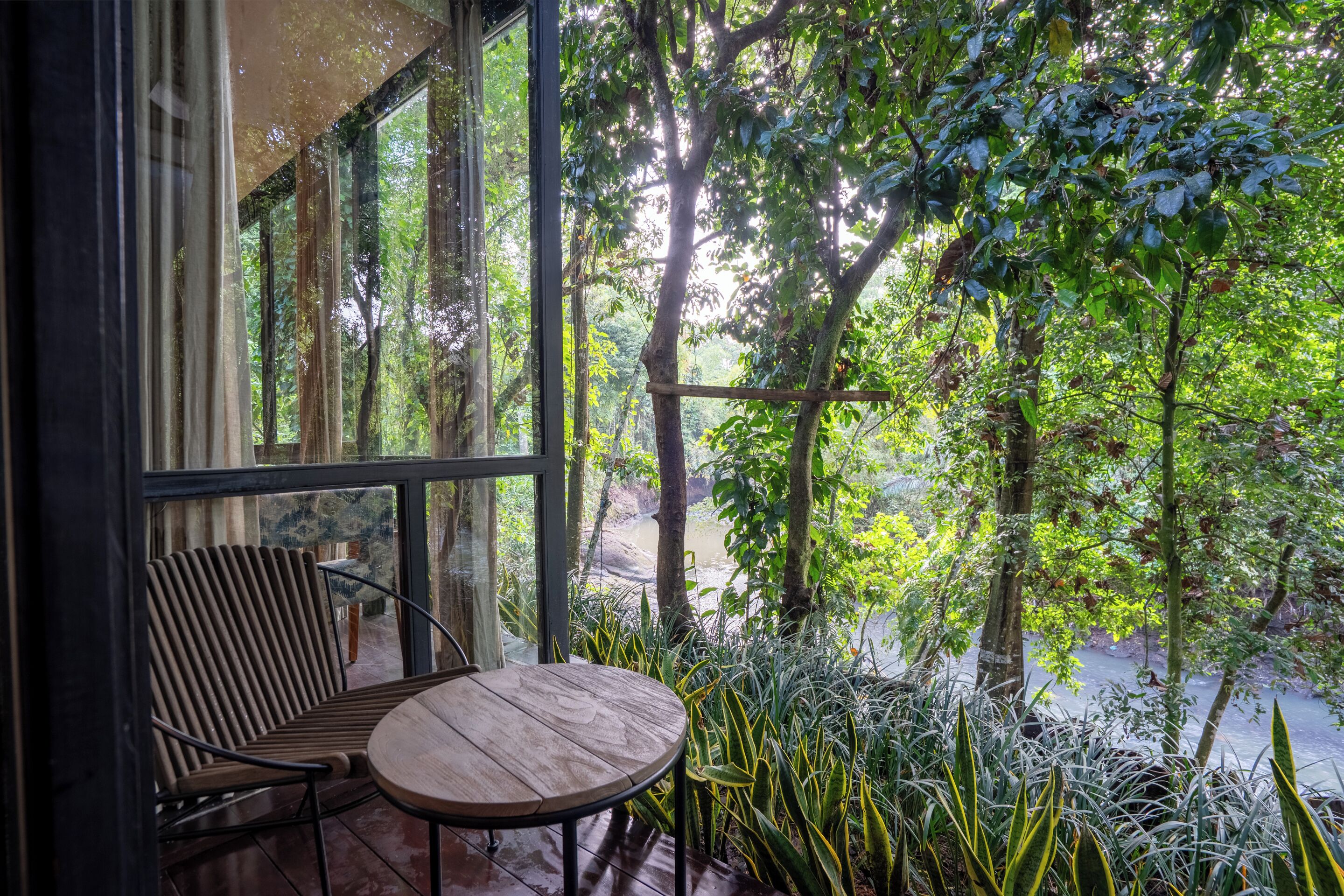 Una silla y una mesa de madera frente a un ventanal con vistas a un jardín exuberante.