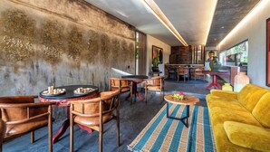 A modern interior with a dining area featuring wooden chairs and a round table, a yellow sofa, and a patterned rug. - Yara Wellness (Buwit)