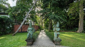 A paved pathway flanked by statues in a garden setting. - Yara Wellness (Buwit)