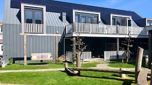 Un bâtiment moderne à deux étages, doté de balcons, d’un banc en bois et d’un petit espace jardin.