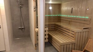 Un sauna avec des bancs en bois et une porte en verre, un espace douche avec une porte en verre et une chaise en bois.