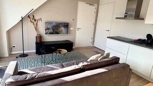 Un salon moderne comprenant un canapé, une table basse, un téléviseur et un coin cuisine avec des placards et un plan de travail.