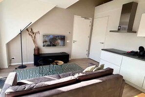 Ein modernes Wohnzimmer mit Sofa, Couchtisch, Fernseher und Küchenzeile mit Schränken und Arbeitsplatte.