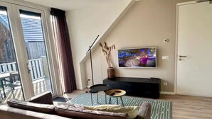 Un salon moderne avec un grand téléviseur, un canapé, une petite table et une vue sur l’extérieur.
