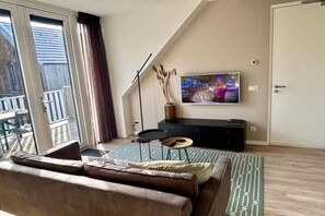 Ein modernes Wohnzimmer mit großem Fernseher, einer Couch, einem kleinen Tisch und Blick ins Freie.