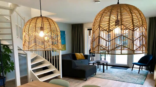Una sala de estar moderna con una escalera, un sofá, una mesa de comedor y dos lámparas de ratán colgantes.