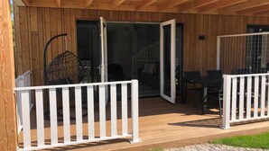 Una terraza de madera con barandilla blanca, un sillón colgante y una mesa con sillas.